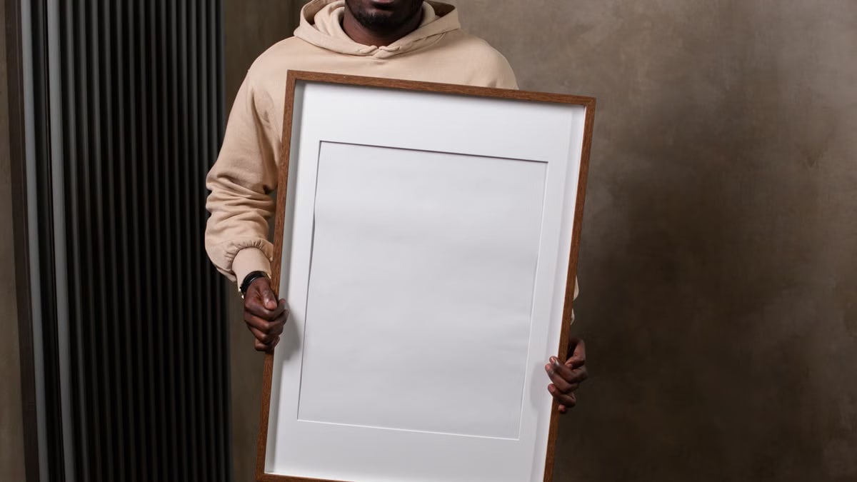 Crop positive African American male demonstrating large empty white frame in modern gray apartment