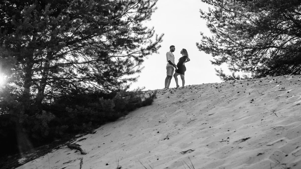 Silhouetted couple standing on a sandy hill surrounded by trees.